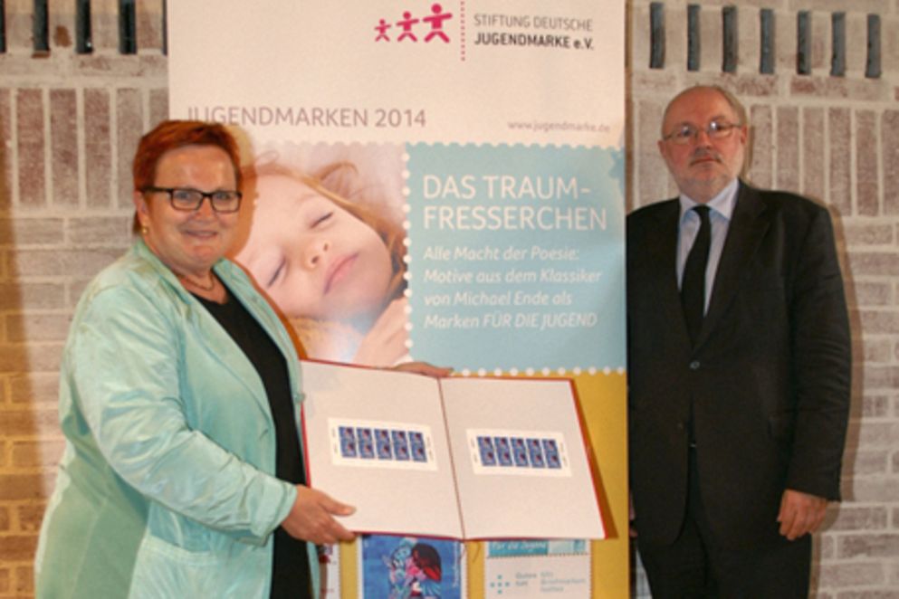Elke Ferner und Michael Sell, Ministerialdirektor im Bundesfinanzministerium, stehen vor dem Banner zur Briefmarkenserie 2014