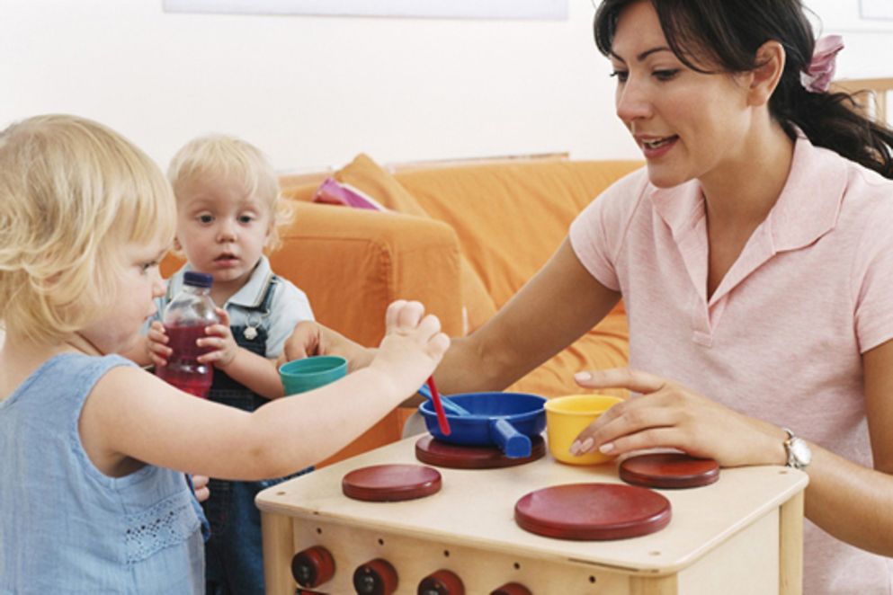 Eine Betreuerin spielt mit zwei Kindern vor einem Spielzeugherd.