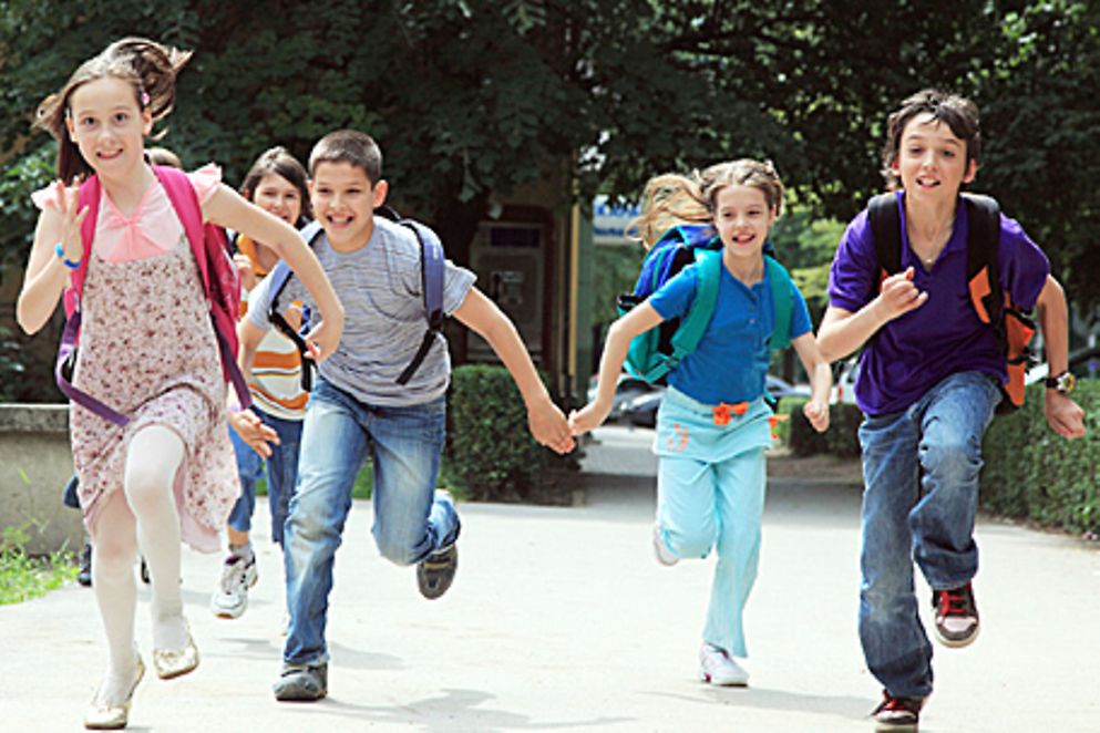 Fünf Schulkinder rennen eine Straße entlang, Bildnachweis: iStock