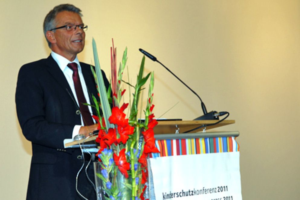 Staatssekretär Josef Hecken steht hinter einem Rednerpult bei der Eröffnung der Kinderschutzkonferenz. Bild: BMFSFJ.