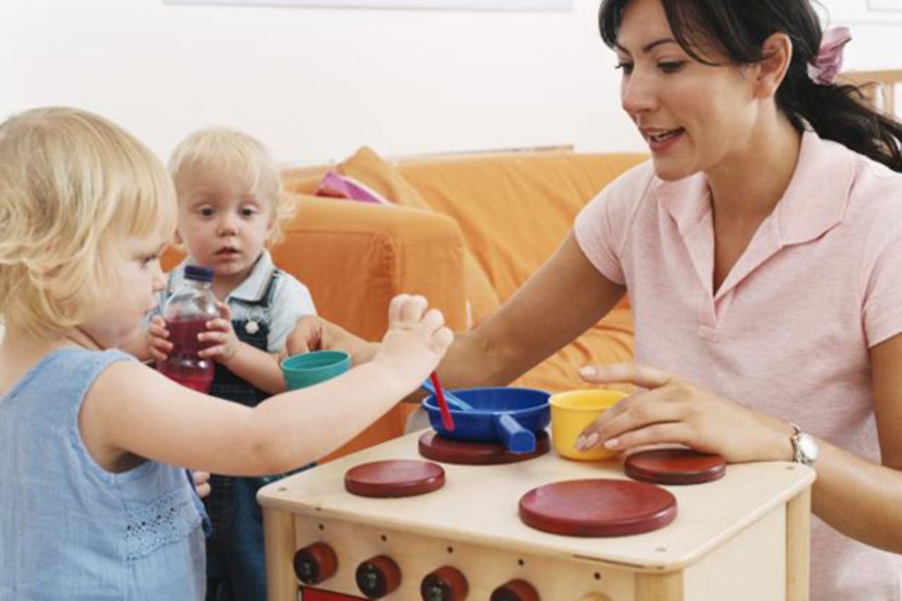 Eine Betreuerin spielt mit zwei Kleinkindern an einem Spielofen, Bildnachweis: BMFSFJ