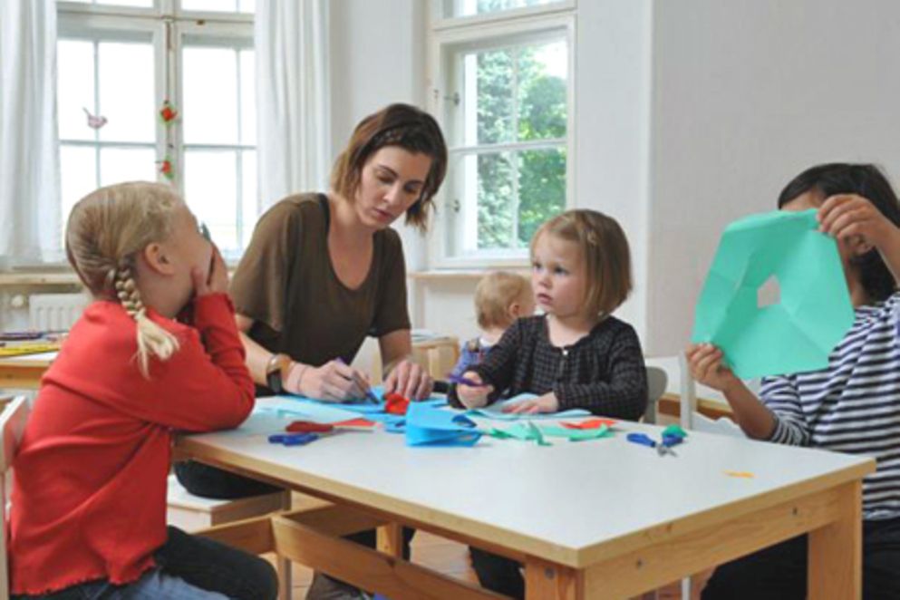 Eine Kindertagespfelgerin spielt mit Kindern an einem Tisch. Bildquelle: Meike Gronau