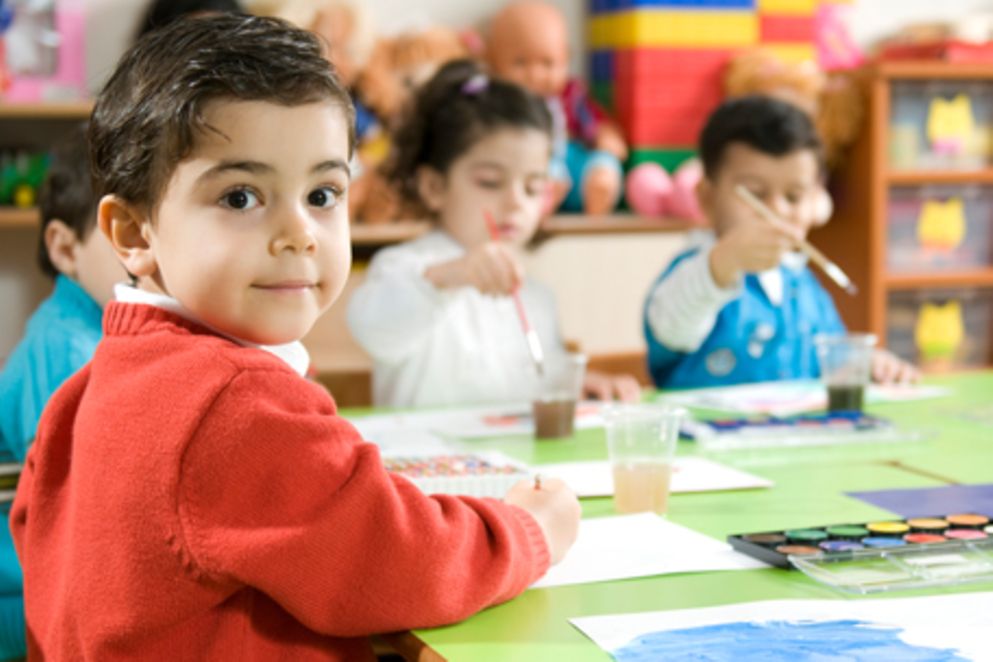 Kind sitz mit anderen Kindern am Tisch und malt. Bildnachweis: iStock