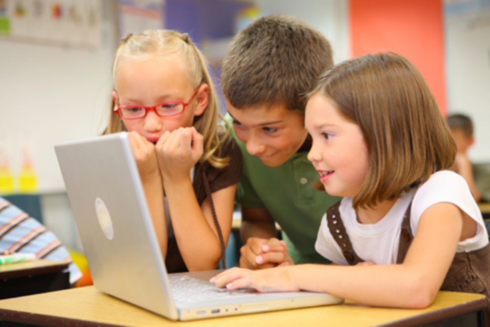 Drei kleine Kinder sitzen vor einem Laptop.