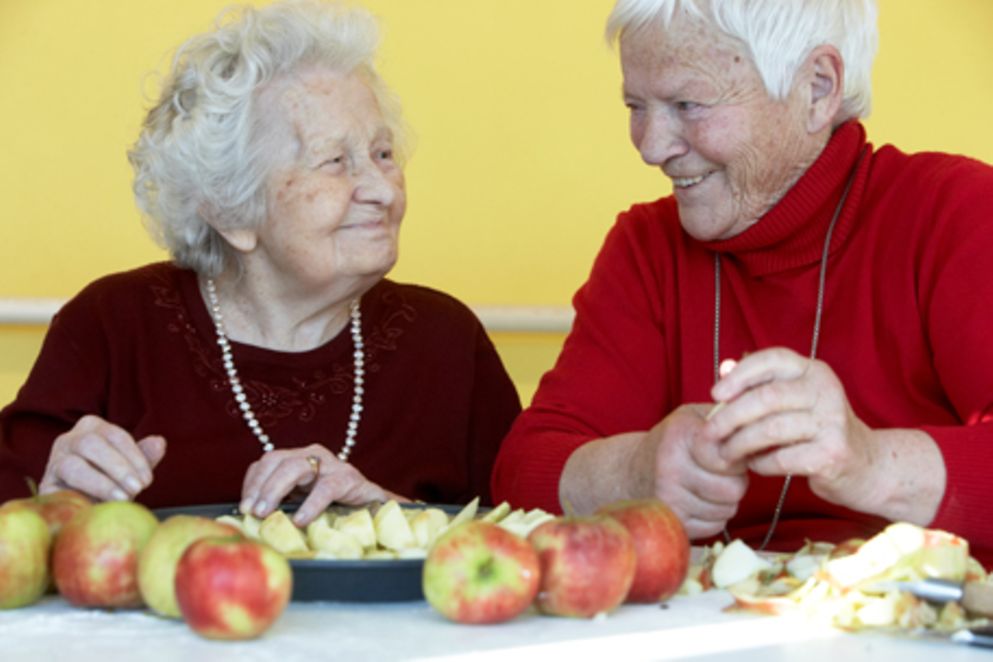 Zwei ältere Frauen sitzen zusammen beim Apfelschälen. Bildnachweis: BMFSFJ