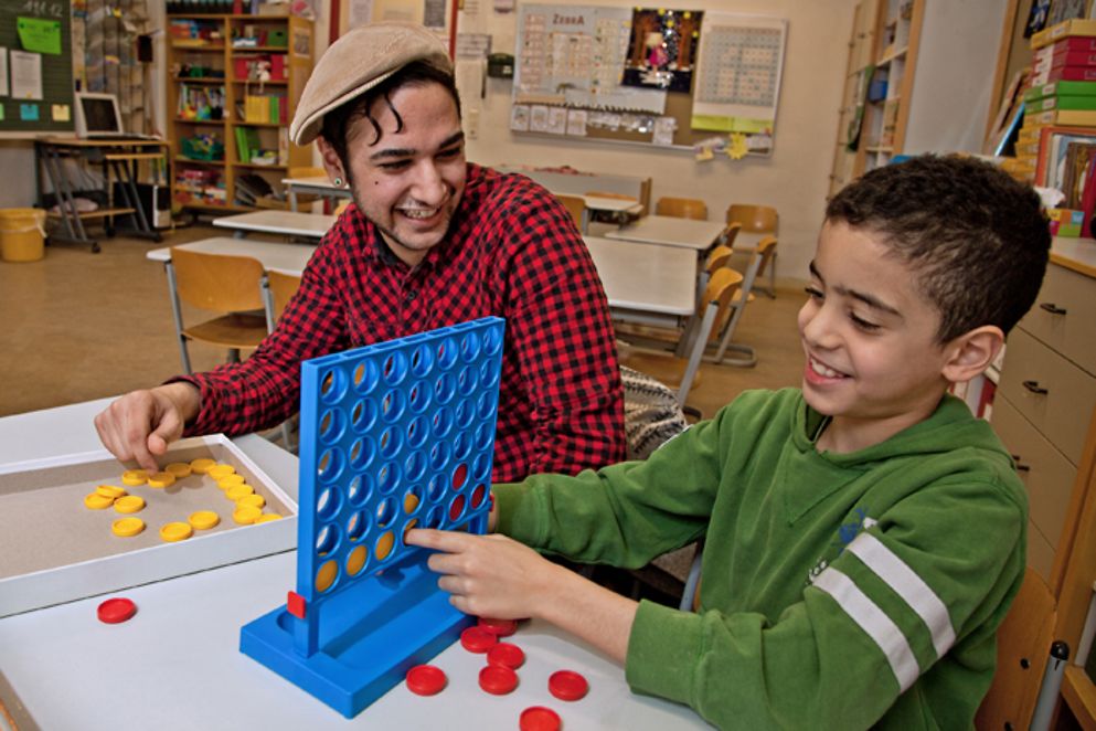 Ein junger Mann spielt ein Tischspiel mit einem Flüchtlingsjungen