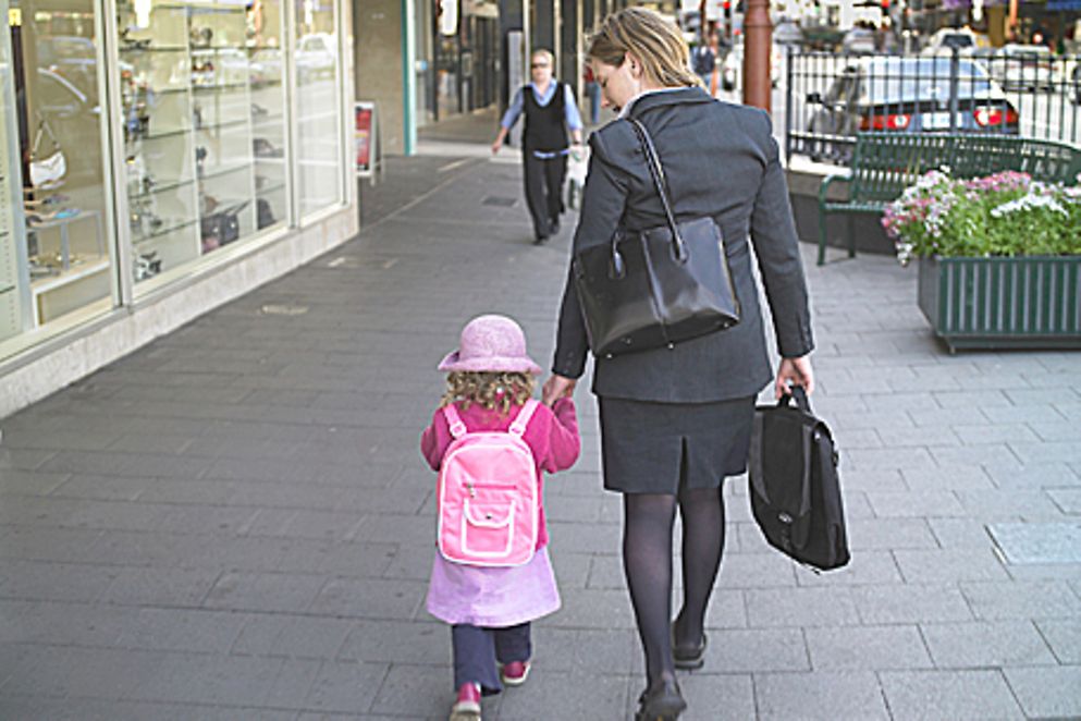 Eine junge Mutter im Businesskostüm läuft mit ihrer Tochter an der Hand auf einer Straße entlang, Bildnachweis: BMFSFJ
