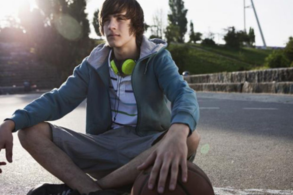 Ein Teenager sitzt mit Kophörern in einem Park