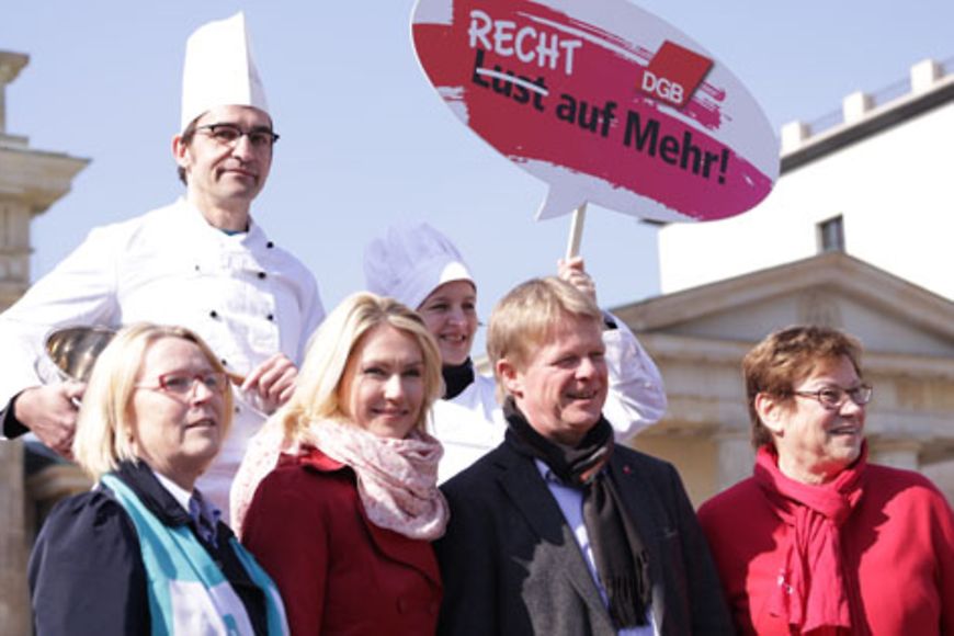 Manuela Schwesig und Reiner Hoffmann in einer Gruppe Menschen, zwei davon als Köche verkleidet