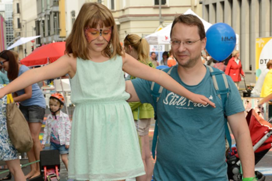 Mädchen balanciert auf einer Slackline, ihr Vater hilft ihr dabei.