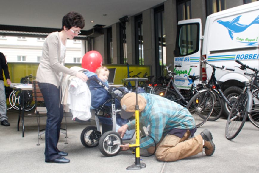 Ein Fahrradmechaniker hockt neben einem Kinderwagen und pumpt Luft auf, Bildnachweis: BMFSFJ