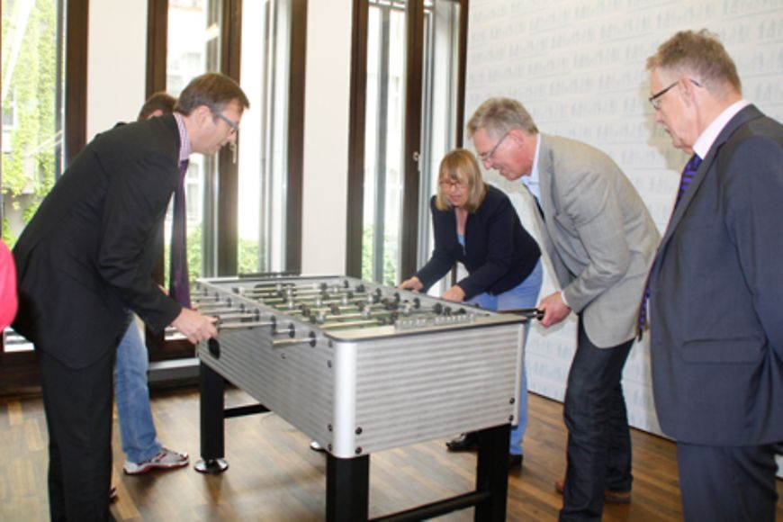 Mitarbeiterinnen und Mitarbeiter spielen an einem Kickertisch oder sehen beim Spiel zu, Bildnachweis: BMFSFJ