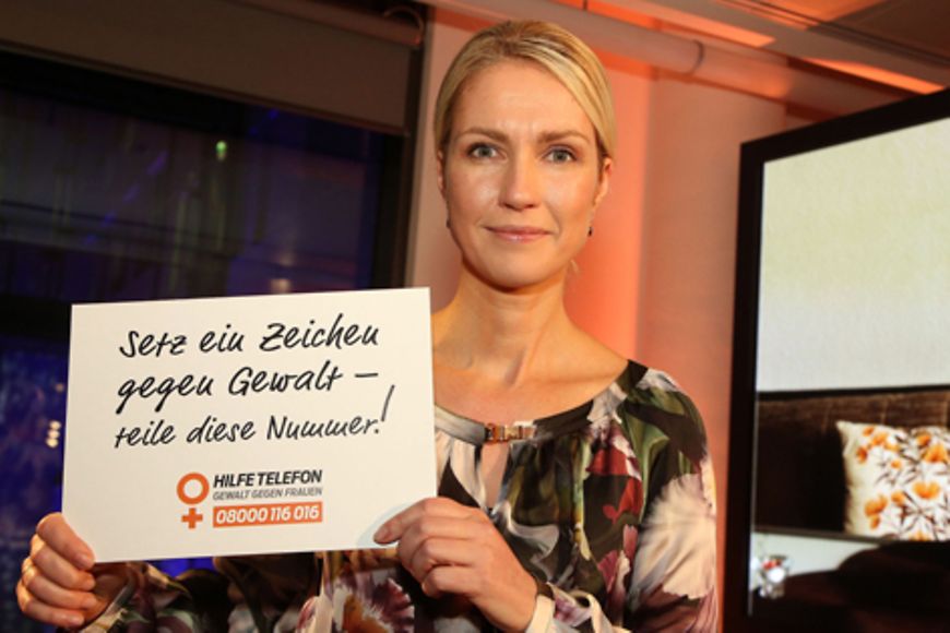 Manuela Schwesig hält ein Schild in der Hand mit der Aufschrift "Setz ein Zeichen gegen Gewalt - wähle diese Nummer"