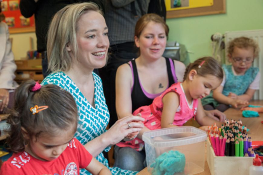 Kristina Schröder sitzt mit spielenden Kindern an einem Tisch, Bildnachweis: BMFSFJ