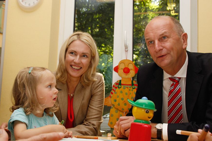 Manuela Schwesig und Dietmar Woidke sitzen gemeinsam mit einem Mädchen an einem Tisch. Das Mädchen malt ein Bild