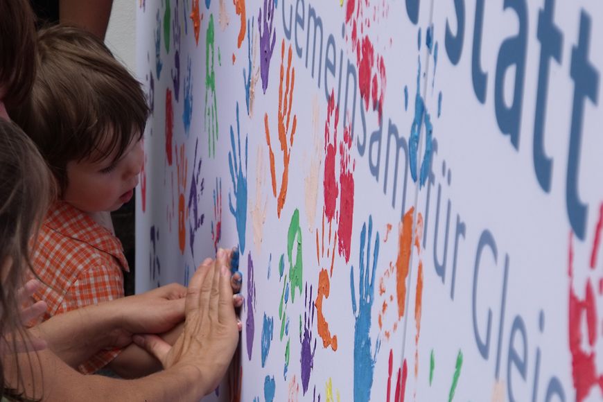 Kinder hinterlassen ihren Handabdruck auf einer Stellwand. Bild: BMFSFJ