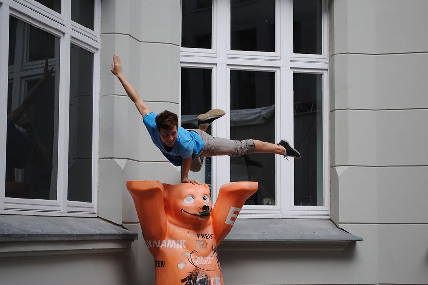 Ein Artist balanciert einhändig auf einer Bären-Statue. Bild: BMFSFJ