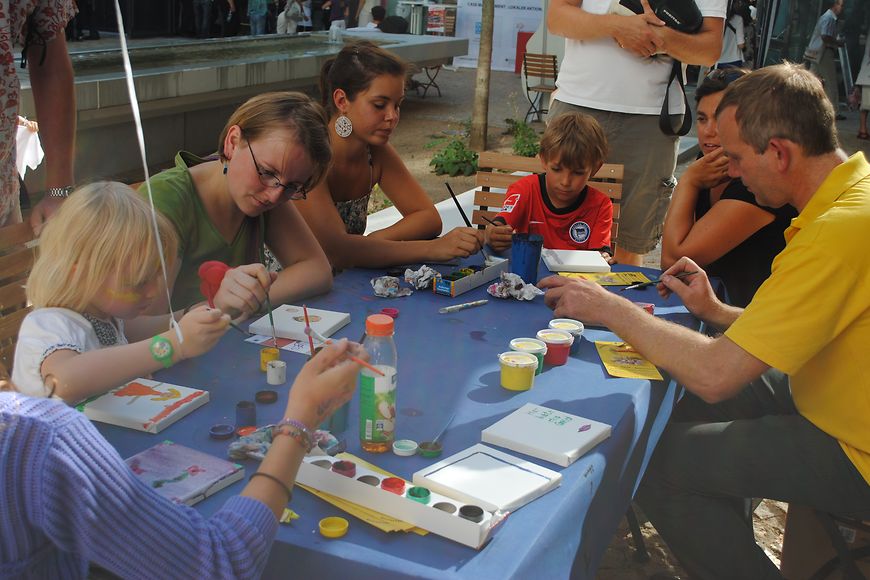 Erwachsene und Kinder sitzen an einem Tisch und malen. Bild: BMFSFJ