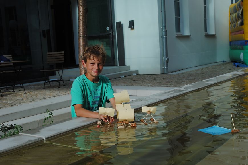 Ein Junge lässt sein Boot auf einem Brunnen schwimmen. Bild: BMFSFJ