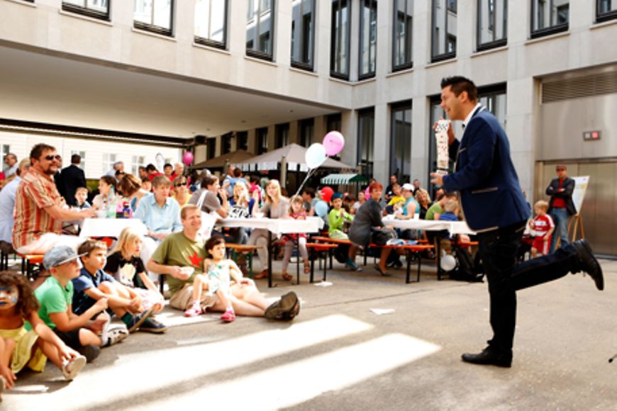 Entertainer steht vor Publikum und vollführt einen Karten-Trick. Bildnachweis: BMFSFJ / Florian Willnauer
